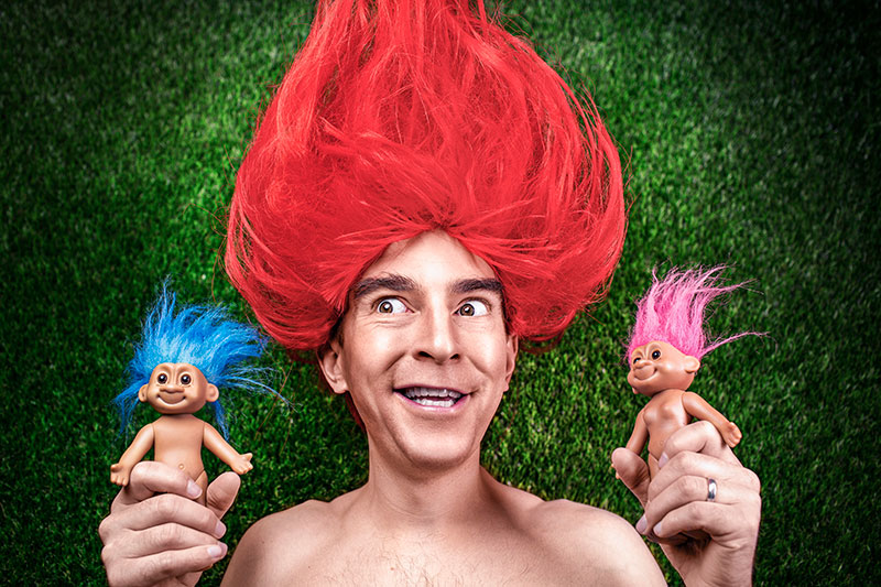 A man with bright red hair holding troll dolls